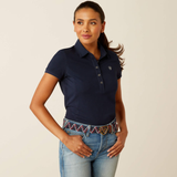 Woman wearing a navy polo shirt and jeans with a belt on a beige background