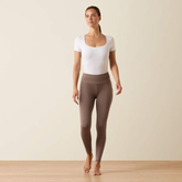 Woman wears a pair of brown riding tights and a white top on a beige background