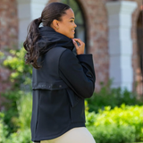 Woman wearing a black jacket outdoors with greenery in the background