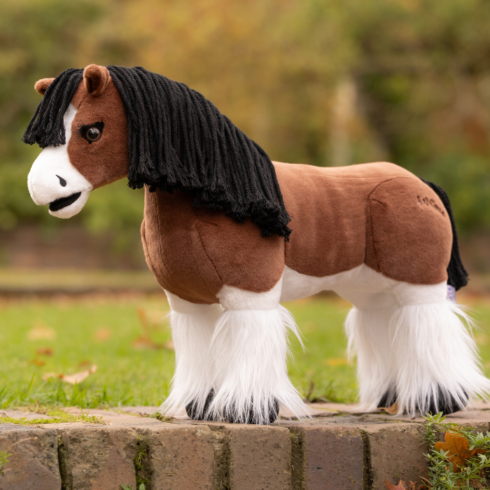 LeMieux AW26 Toy Pony Variant Colour Titan. A plush toy pony brown and white wirh black wool mane on faded garden background. 