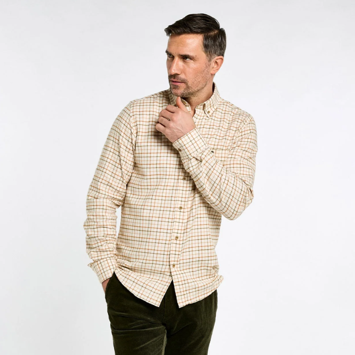 Dubarry Men's Corrib Shirt Variant Ochre. A man wearing a beige and brown checkered long-sleeve button-down shirt and dark green trousers, posing against a light gray studio background.