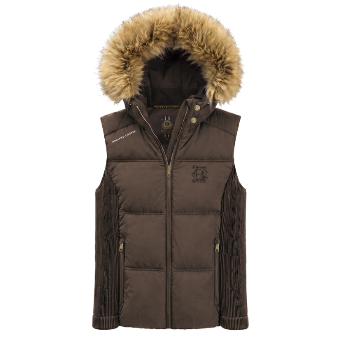 Holland Cooper Cranborne Training Gilet Variant Chocolate. A dark brown puffer vest with a large tan faux-fur trimmed hood, featuring a front zipper, ribbed knit sleeves, and a tonal embroidered crest logo on the left chest.