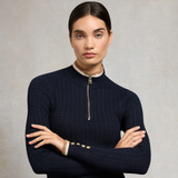 Lady wearing a Navy jumper with gold buttons and beige/cream detailing against a grey background. 