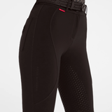 Close-up of brown equestrian riding breeches with textured grip panels on the seat and upper thigh, a small red brand tab, and a matching black patterned belt, shown against a light grey studio background.