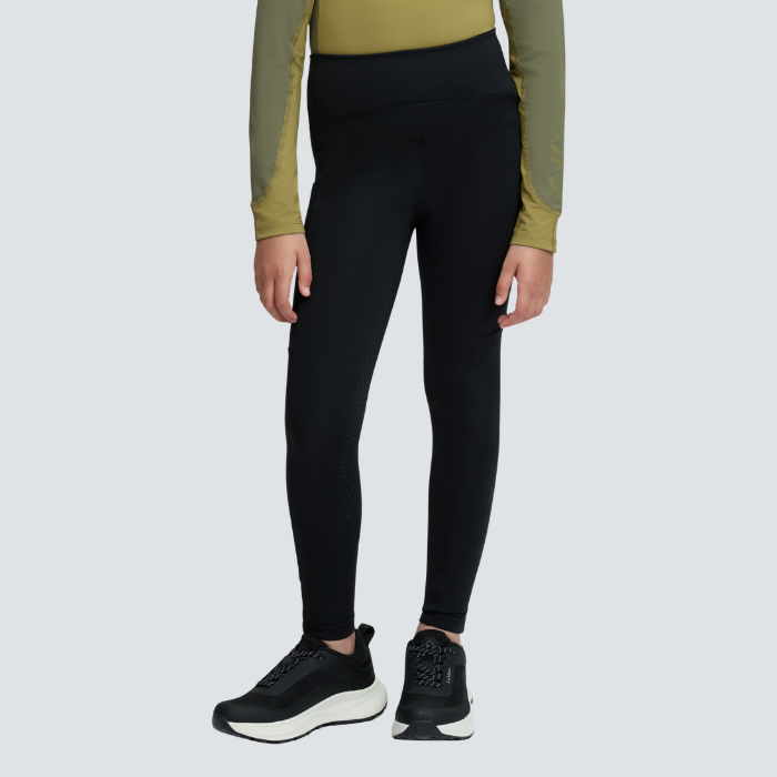 Child wearing black trousers and a green base layer agaisnt a white background. 