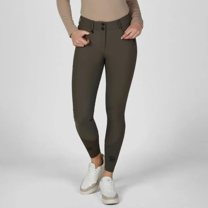 Pikeur AW26 Ceelina Matrixgriptex Breeches Variant Deep Khaki. A model wearing dark olive green riding breeches with a beige long-sleeve top and white sneakers, shown from the waist down against a light gray studio background. 