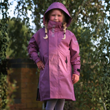 A young girl wearing a purple hooded raincoat with a high collar and drawstrings, standing outdoors in front of a blurred background of trees.