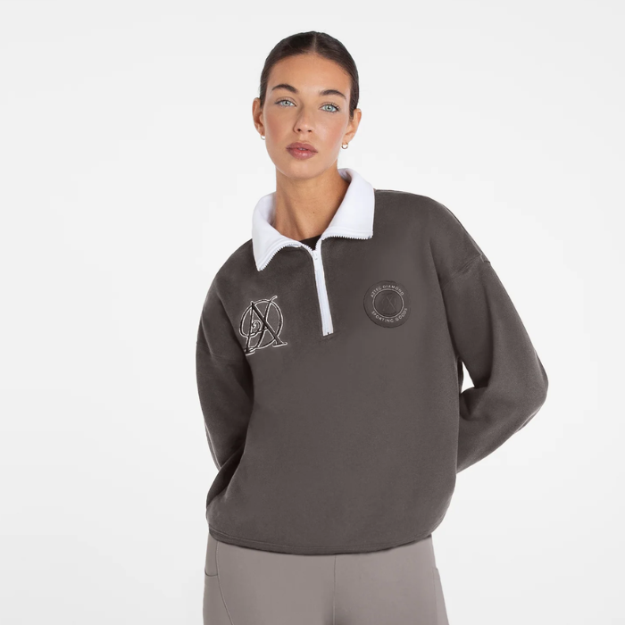 A woman modeling a dark brown quarter-zip sweatshirt with a white collar. The sweatshirt features a circular logo on the left chest and a stylized 'AD' logo on the right chest.