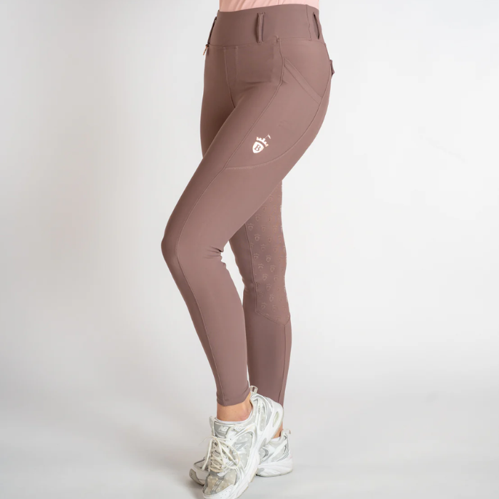 A person wearing high-waisted athletic leggings in a dusty mauve-brown color, paired with white sneakers, shown from the waist down against a light gray studio background.