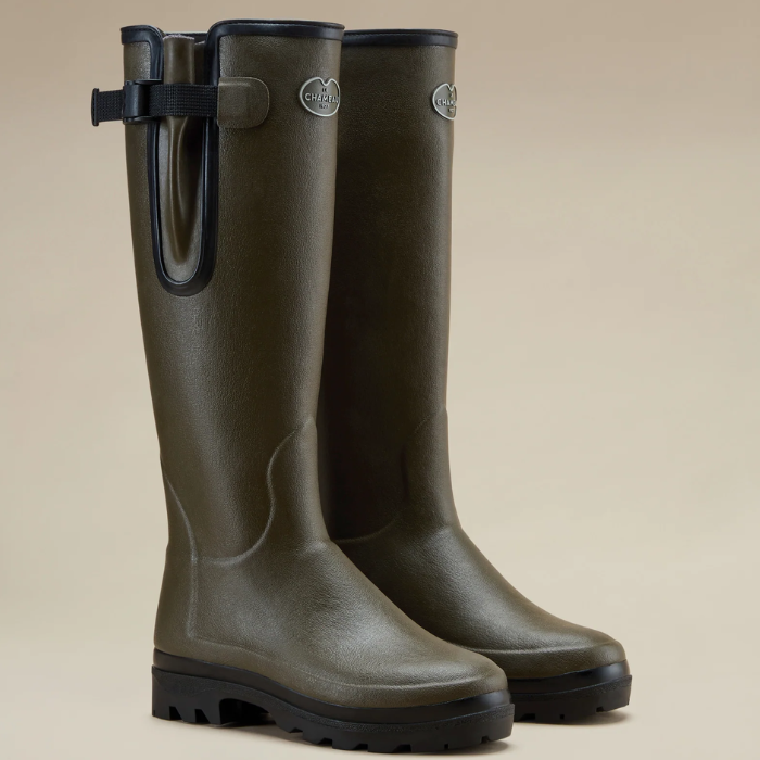 Le Chameau Ladies Vierzonord Neoprene Lined Wellies Variant Chameau Green. A pair of dark olive green rubber rain boots with black soles and a black strap detail on the outer side, displayed against a solid beige background.