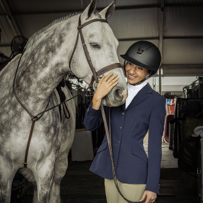 Woman in equestrian attire petting a gray horse in a stable.