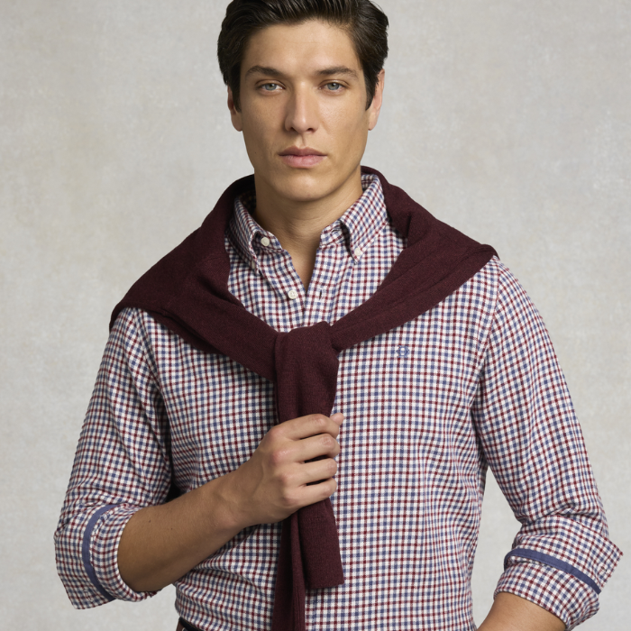 Holland Cooper Men's Classic Fit Brushed Cotton Shirt Variant portland Red Check. A man wearing a red and white checkered button-down shirt with a dark burgundy knit sweater draped over his shoulders, photographed against a neutral textured gray background.