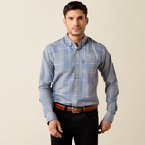 Ariat Men's Clement Long Sleeve Shirt Varient Soft Blue Plaid. A man wearing a light blue long-sleeve plaid button-down shirt with a brown belt and black pants, standing against a plain beige background.