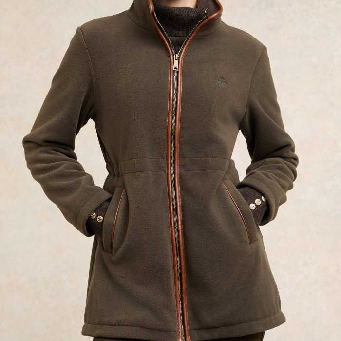 Holland Cooper Country Longline Fleece Varient Khaki. A dark brown fleece jacket with a full front zipper, contrasted with a thin orange-brown trim, worn by a model. The jacket features a stand-up collar, zippered hand pockets, and a small embroidered logo on the left chest.