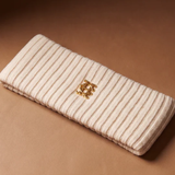 A cream-colored ribbed headband with a Gold HC logo on a Brown background.