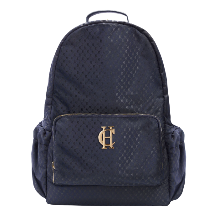 Holland Cooper Burghley Backpack Variant Ink Navy Monogram. A dark navy blue backpack with a subtle repeating monogram pattern, featuring a front zippered pocket with a gold-tone 'HC' logo and side pockets, set against a plain white background.