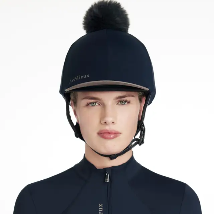 Person wearing a navy equestrian helmet with a pom-pom on a white background