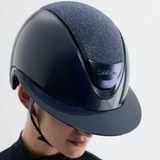 Dark gray riding helmet with glittery top worn by a person on a light gray background