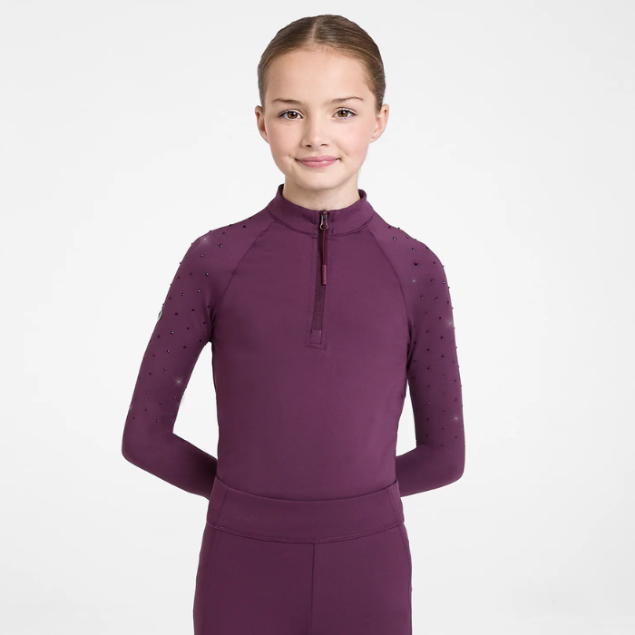 Young girl wearing a Plum base layer with crystal embellishments on the shoulder against a grey background. 