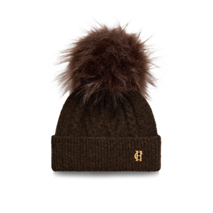 Holland Cooper Sloane Cable Bobble Hat Variant Chocolate. A dark brown cable-knit beanie with a large matching faux fur pom-pom and a small gold embroidered 'H' logo on the front cuff, shown against a plain white background.