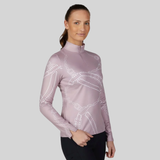 Pikeur AW26 Zip Print Shirt Collection Variant Ash Mauve. A woman modeling a long-sleeve athletic quarter-zip top in dusty lavender with white dotted chain and bow patterns, paired with black riding pants, against a solid gray studio background.