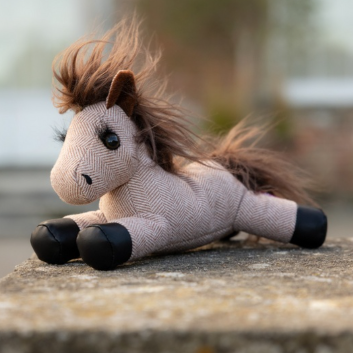 LeMieux AW26 Tiny Beanie Pony Rosie Varient Brown. Mini striped toy pony with black hooves and a brown fluffy main on a brick wall. 