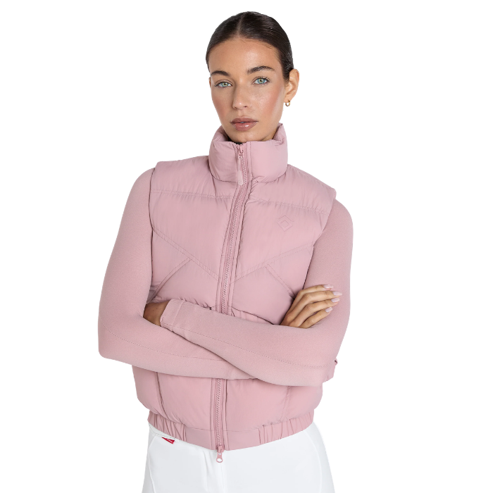 A woman modeling a light pink sleeveless puffer vest with a high stand-up collar and front zipper, paired with white pants, against a solid white background.