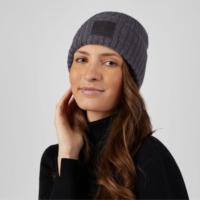 Pikeur Beanie Selection 285800 Variant Basalt Grey. A woman wearing a dark gray ribbed knit beanie with a black rectangular logo patch on the front, posed against a light gray studio background.