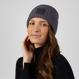 Pikeur Beanie Selection 285800 Variant Basalt Grey. A woman wearing a dark gray ribbed knit beanie with a black rectangular logo patch on the front, posed against a light gray studio background.