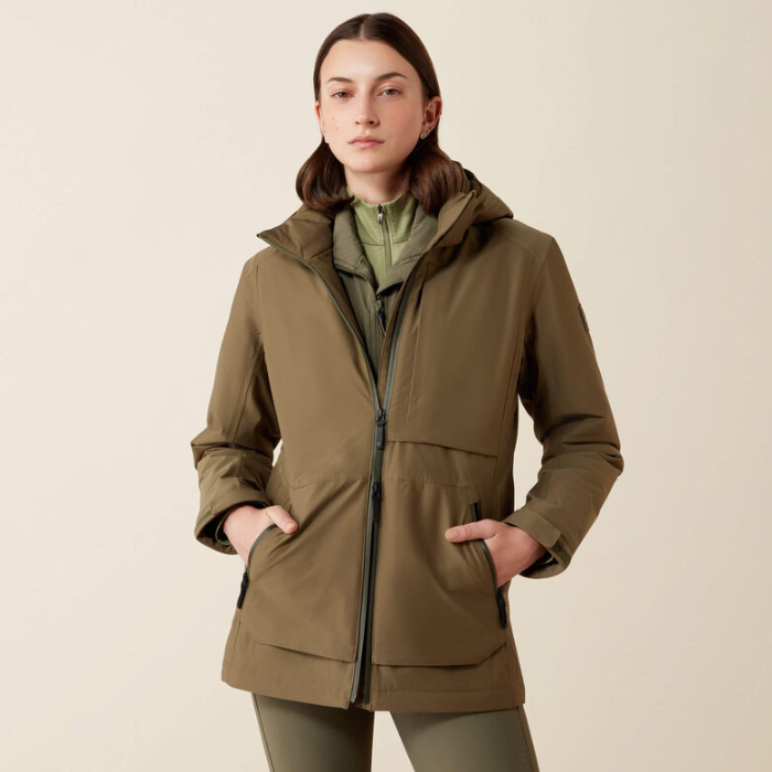 Lady wearing a olive coloured jacket with a dark green zip and big pockets against a beige background. 