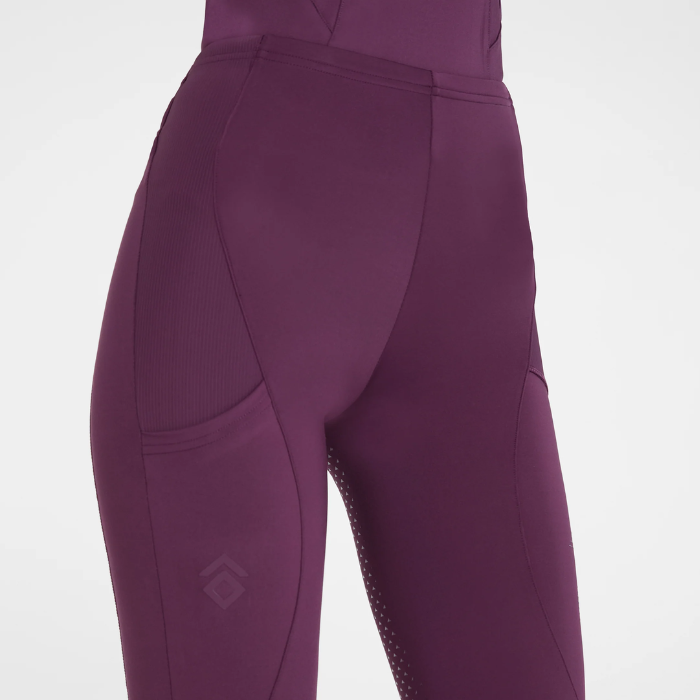 Aztec Diamond AW26 Core Leggings Full Seat Variant Plum. Close-up of a person wearing fitted athletic leggings in a deep plum-purple color, showing the side and back fit with a subtle tonal logo near the lower leg on a light gray background.