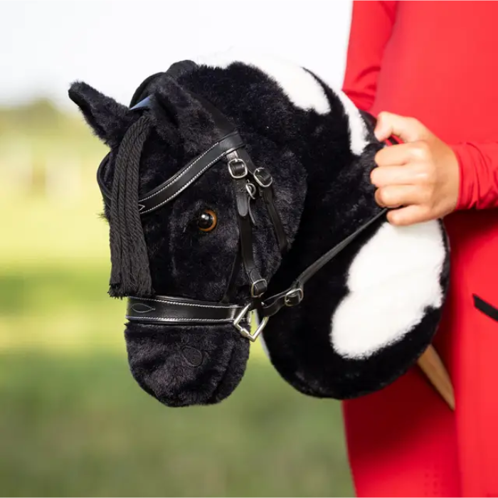 Black and white plush horse held by a person in a red coat with a blurred green background