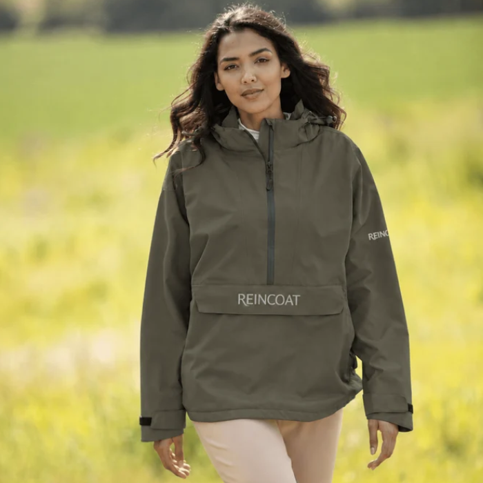 Reincoat Smock Pro Variant Olive. Lady standing in a field wearing a Olive jacket with 'REINCOAT' on the front. 