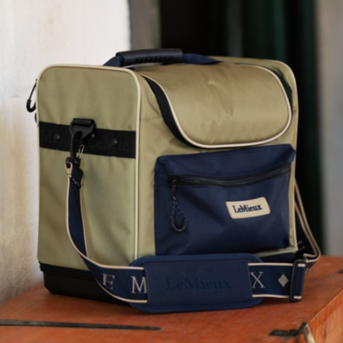 LeMieux AW26 Elite Pro Grooming Bag Varient Gooseberry. A LeMieux soft-sided cooler bag in olive green and navy blue, resting on a wooden surface against a neutral indoor background.