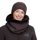 A smiling woman wearing a dark brown cable-knit beanie, a matching fuzzy knit neck warmer, and a fleece jacket against a plain white background.