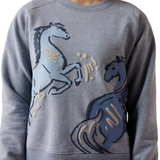 Ariat Youth Martine Sweatshirt AW26 Varient Blue Grey Lets Play. Close up of a blue jumper with two horses, one in dark blue and one in baby blue with white detailing. 