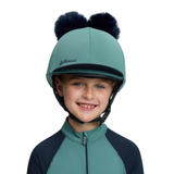 LeMieux AW26 Mini Double Pom Hat Silk Variant Colour Navy/Aloe.
A smiling child wearing a mint green and navy equestrian helmet with two dark faux-fur pom-poms on top, paired with a matching mint and navy long-sleeve jersey against a plain white background.