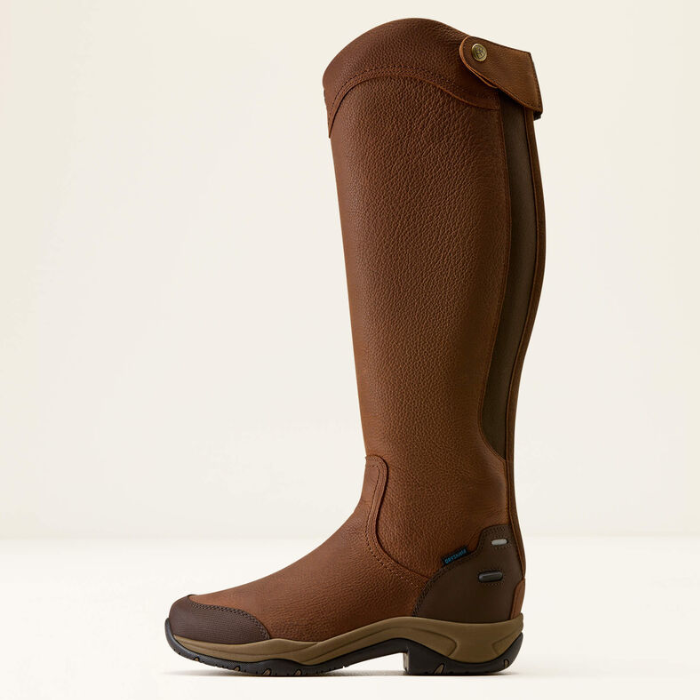 A tall brown leather riding boot shown in a side profile against a clean, off-white background. The boot features a textured brown leather shaft, darker brown side panels, a brown leather toe cap, and a low brown heel with a black outsole.