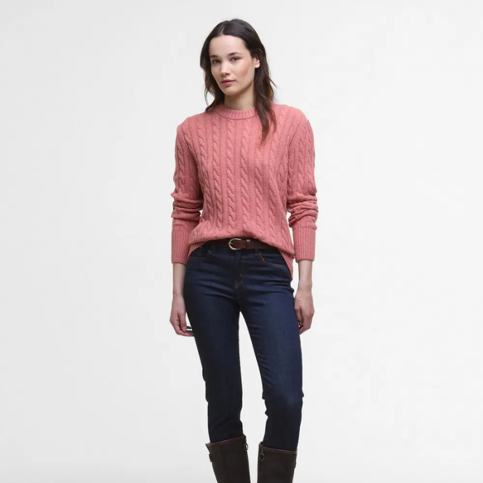 Woman wearing a pink jumper and dark jeans on a white background