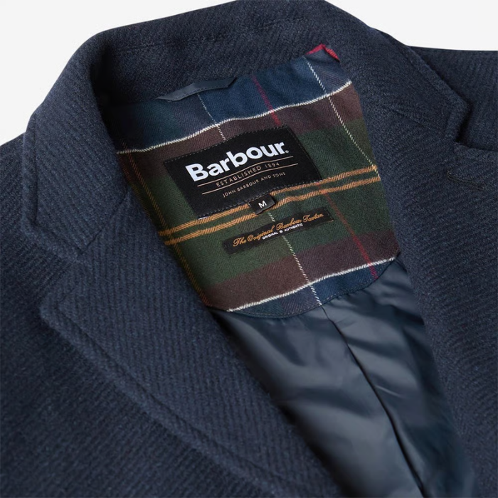 Close-up of a navy wool-blend coat lapel and collar with a Barbour plaid inner lining and visible Barbour branding label.