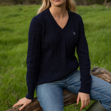 LeMieux AW26 Cora Cable V-Neck Knit Jumper Variant Colour Navy. Lady in navy jumper and jeans on faded grass background.