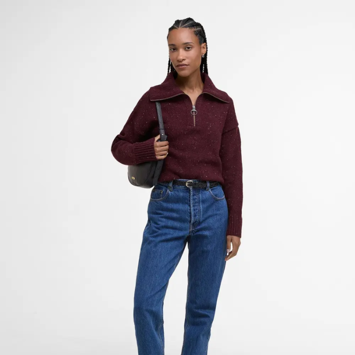 Woman wearing a burgundy knitted jumper and blue jeans on a white background