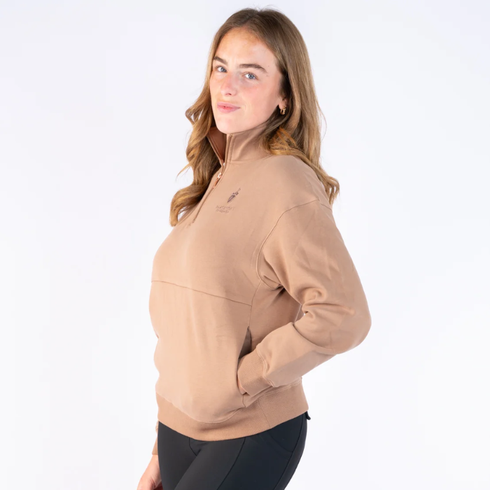 Blackfort Equestrian Ella Quarter Zip Variant Caramel. A woman modeling a light tan quarter-zip pullover sweatshirt with a small embroidered logo on the left chest, paired with black leggings, against a plain white studio background.
