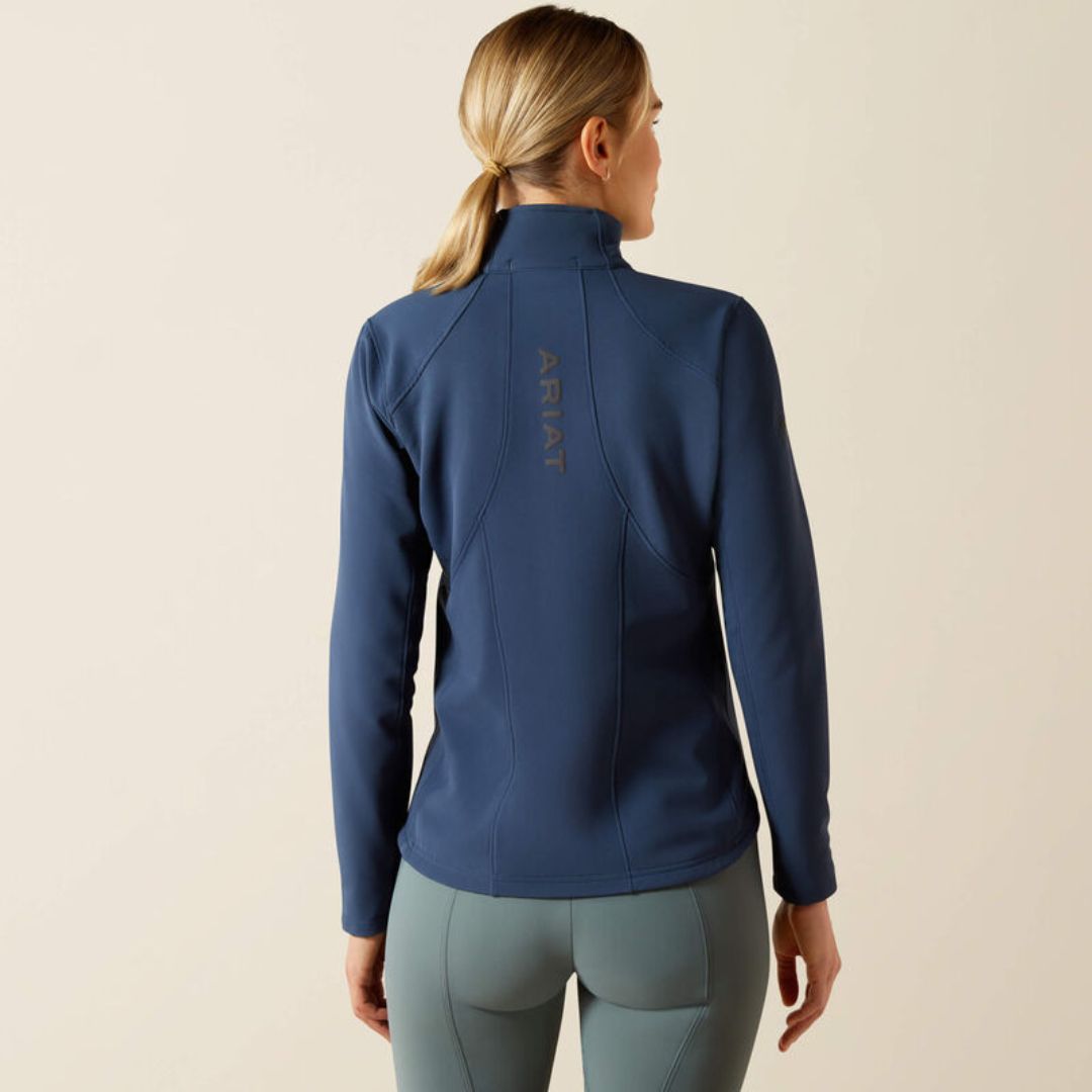 person wears a navy blue jacket with ARIAT logo on the back on a neutral background