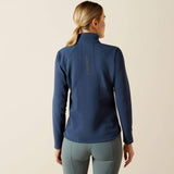person wears a navy blue jacket with ARIAT logo on the back on a neutral background