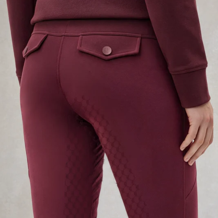 Close-up back view of a person wearing burgundy fitted leggings with a quilted pattern on the upper thighs and a flap pocket with a button at the waist, paired with a matching long-sleeve top against a light gray background.