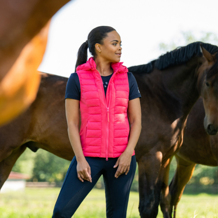 Female model wearing pink gillet with bay horse in back ground
