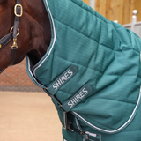 A close-up of a horse wearing a teal green quilted horse blanket with white piping and teal straps. The brand name 'SHIRES' is clearly visible on two of the straps.