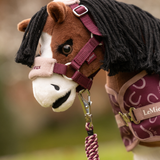 LeMieux AW26 Toy Pony Vogue Headcollar & Leadrope Variant Colour Blackberry. A close up of a plush toy pony wearing a headcollar and leadrope in blackberry colour withe white faux fur trim on faded garden background