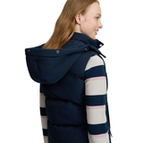 LeMieux AW26 Margot Hooded Gilet Varient Navy. Woman wearing a Navy hooded gilet with a stripy top undeneath and a large hood with the option of adding fur. 
